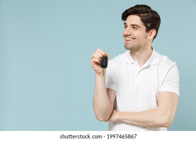 Young happy smiling fun caucasian man 20s in white casual basic t-shirt hold in hand cark key fob keyless system look aside isolated on pastel blue background studio portrait People lifestyle concept.
