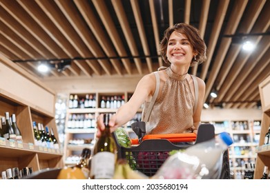 Young Happy Smiling Fun Cheerful Woman 20s In Casual Clothes Shopping At Supermaket Store Hold White Wine Alcohol Put Bottle In Grocery Cart Inside Hypermarket Purchasing Gastronomy Lifestyle Concept