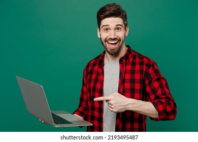 Young happy smiling fun cool man he 20s wearing red shirt grey t-shirt hold use work point index finger on laptop pc computer isolated on plain dark green background studio. People lifestyle concept - Powered by Shutterstock