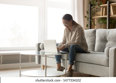 Young happy smiling mixed race woman working with computer in living room, chatting with friends, dating online, shopping, writing blog. Millennial motivated student studying, preparing for exam.