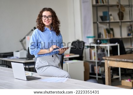 Young happy smiling professional business woman, female company worker or corporate manager holding digital tablet technology posing in modern office working, looking at camera, portrait.