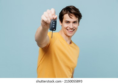 Young happy smiling satisfied cheerful caucasian man 20s in yellow t-shirt holding give car keys keyless system isolated on plain pastel light blue background studio portrait. People lifestyle concept