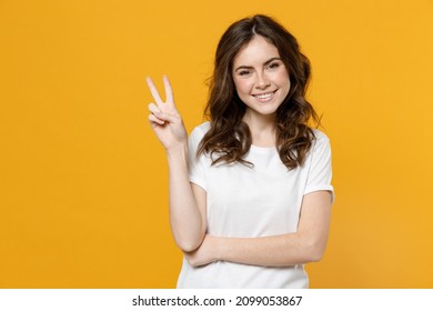 Young happy smiling satisfied positive fun eueropean caucasian student woman 20s in white basic casual t-shirt show victory v-sign gesture isolated on yellow orange color background studio portrait
