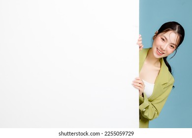 Young happy smiling successful employee business woman 20s in casual green jacket peeking out blank whiteboard isolated on pastel blue background. Female entrepreneurs, office worker concept.