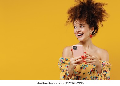 Young Happy Smiling Woman 20s With Culry Hair In Casual Clothes Use Hold Mobile Cell Phone Look Aside On Copy Space Workspace Area Isolated On Plain Yellow Background Studio. People Lifestyle Concept