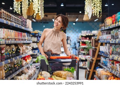 Young happy smiling woman 20s wearing casual clothes shopping at supermaket store buy choosing pasta products browsing with grocery cart inside hypermarket People purchasing gastronomy food concept - Shutterstock ID 2243253991