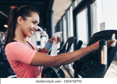 Young happy and smiling woman cleaning and weeping expensive fitness gym equipment with sprayer and cloth. - Powered by Shutterstock