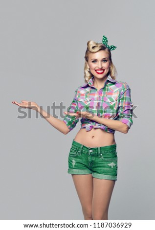 Young happy smiling woman, dressed in pin-up style, showing something or copyspace area for advertise, slogan or text message. Caucasian blond model posing in retro fashion and vintage concept.