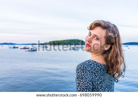 Young happy smiling woman sitting on edge of dock in Bar Harbor, Maine looking over shoulder