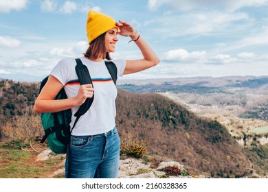 Young happy smiling woman, wears yellow beanie and backpack, hiking in the mountains. Top view, landscape, adventure concept.