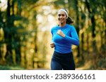 Young happy sportswoman with earbuds running in the park. Copy space.