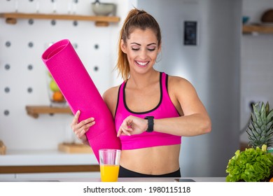 Young Happy Sportswoman Looking At Time On Her Wristwatch While Drinking Detox Smoothie In The Kitchen. My Health Stats Are Perfect. Young Sports Woman Measuring Tracing Pulse On Smart Watch