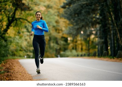 Young happy sportswoman running on the road in nature. Copy space.