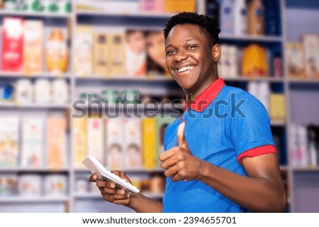 young happy store keeper holding and using calculator while giving thumbs up for approval