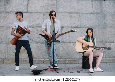 Young And Happy Street Musicians Band With Guitars And Djembe In City