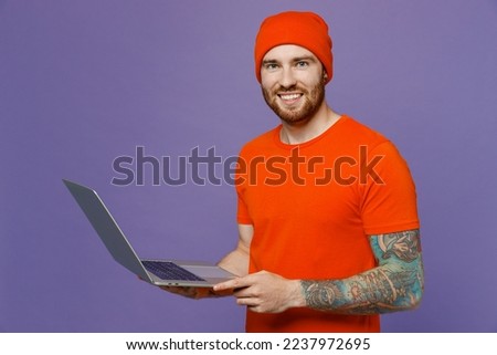 Young happy student freelancer IT man 20s he wear red hat t-shirt hold use work on laptop pc computer look camera smile isolated on plain pastel light purple background studio People lifestyle concept Foto stock © 
