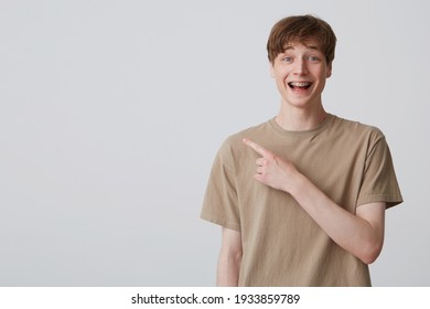 young happy student wears beige t-shirt indicates with finger into copy space. isolated over white background. young guy points with a finger into left side