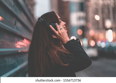 Young happy stylish trendy casual hipster woman teenager listening to music on a wireless headphone while walking around the city. Music lover enjoying music