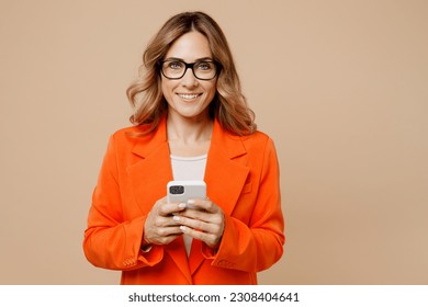 Young happy successful employee business woman corporate lawyer 30s wear classic formal orange suit glasses work in office hold in hand use mobile cell phone isolated on plain beige background studio - Powered by Shutterstock