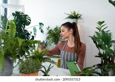 Young Happy Successful Woman Florist In Her Flowershop Surrounded With Flowers In Flowerpots Working Job She Love As Small Business Owner. Carefree Female Gardener Surrounded With Green Plants.