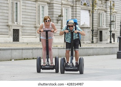 Young Happy Tourist Couple Riding Segway Enjoying City Tour In Madrid Palace In Spain Having Fun Driving Together On Funny And Romantic Summer Holiday In Urban Transport Concept