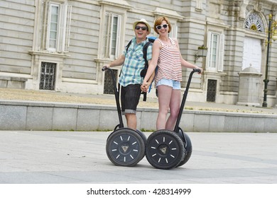 Young Happy Tourist Couple Riding Segway Enjoying City Tour In Madrid Palace In Spain Having Fun Driving Together On Funny And Romantic Summer Holiday In Urban Transport Concept