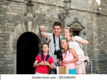 Young Happy Tourist Family Of Four Strolling On City Streets And Taking Selfie