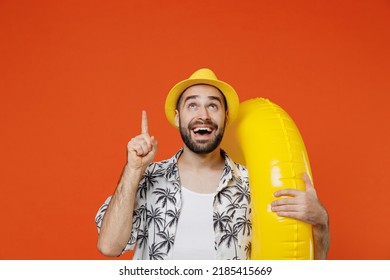 Young Happy Tourist Man In Beach Shirt Hat Hold Inflatable Ring Point Index Finger Overhead On Workspace Isolated On Plain Orange Background Studio Portrait. Summer Vacation Sea Rest Sun Tan Concept