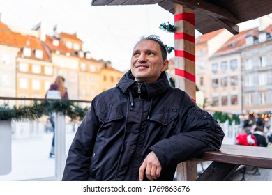 Young Happy Tourist Man In Warsaw, Poland Old Town Market Square Rynek In Warszawa Christmas Decorations With People Skating In Ice Rink