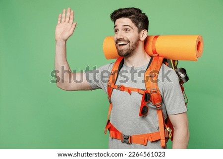 Young happy traveler white man carry backpack stuff mat waving hand isolated on plain green background. Tourist leads active healthy lifestyle walk on spare time. Hiking trek rest travel trip concept