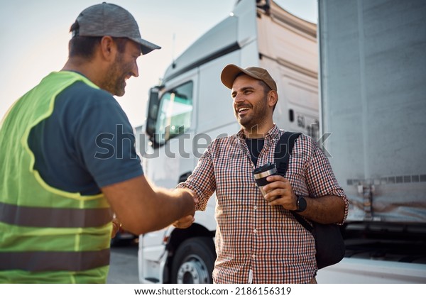 Young happy truck driver shaking hands with a\
dispatcher on parking\
lot.