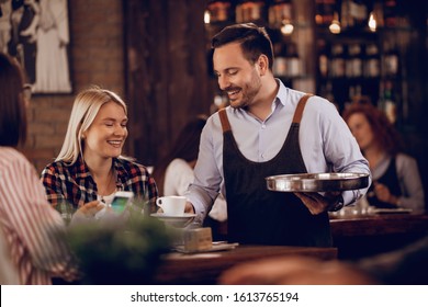 Young happy waiter serving coffee to female customers in a bar.  - Powered by Shutterstock