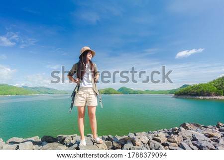 Young happy woman with backpack standing with raised hands and looking to the river. Woman traveling concept