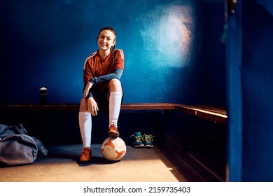 Young happy woman with ball sitting in dressing room before soccer match and looking at camera. Copy space. - Powered by Shutterstock