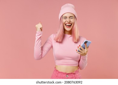 Young happy woman with bright dyed rose hair in rosy top shirt hat hold in hand use mobile cell phone do winner gesture isolated on plain light pastel pink background People lifestyle fashion concept. - Powered by Shutterstock