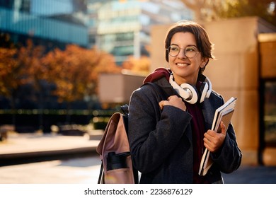 Young happy woman carrying backpack and books while going on a lecture at campus.  - Shutterstock ID 2236876129