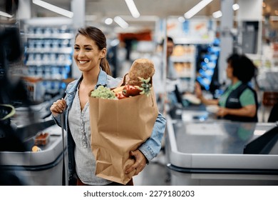 Young happy woman carrying paper bag with groceries after shopping in supermarket.  - Powered by Shutterstock