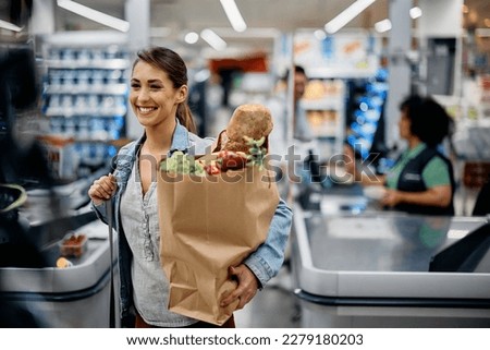Young happy woman carrying paper bag with groceries after shopping in supermarket. 