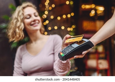 Young happy woman in casual clothes at cafe buy breakfast sit at table hold wireless modern bank payment terminal to process acquire credit card payments relax in restaurant during free time indoors.