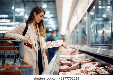 Young happy woman choosing fresh meat while buying food at the supermarket.  - Powered by Shutterstock