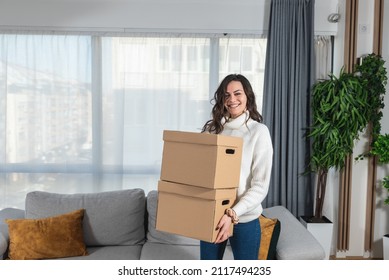 Young Happy Woman College Student Moving In In Her New Modern Studio Apartment. Businesswoman Holding Cardboard Boxes With Stuff Rented New Home After She Got Promoted At Work.