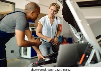 Young happy woman communicating with her auto repairman who is examining engine problems in a workshop.  - Powered by Shutterstock