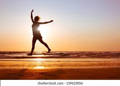 Young happy woman dancing on the beach at sunset with sea background, silhouette