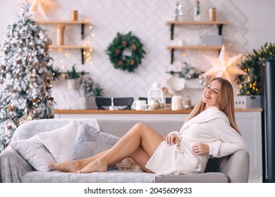 Young Happy Woman In A Dressing Gown, Sitting, Posing, Smiling, Resting In A Room Decorated With A Christmas Tree