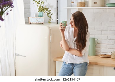 Young happy woman drinking coffee on the kitchen in the morning