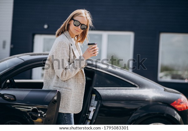 Young happy woman
drinking coffee by the
car