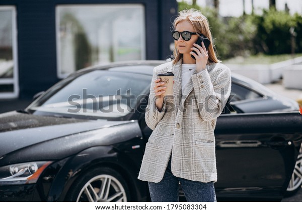 Young happy woman\
drinking coffee by the\
car