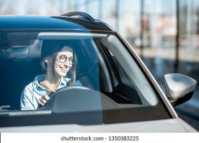 Young And Happy Woman Driving A Luxury Car, Front View Through The Windshield With Sunlight