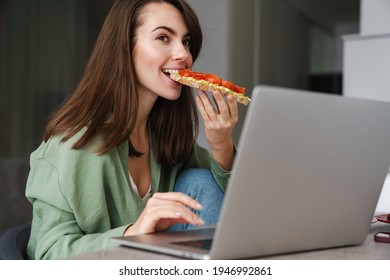 Young Happy Woman Eating Avocado Toast While Working With Laptop At Home Kitchen