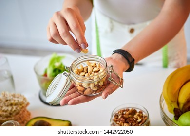 Young Happy Woman Eating Different Nuts (cashew, Hazelnut, Almond) In Modern Kitchen. Healthy Food And Dieting Concept. Loosing Weight